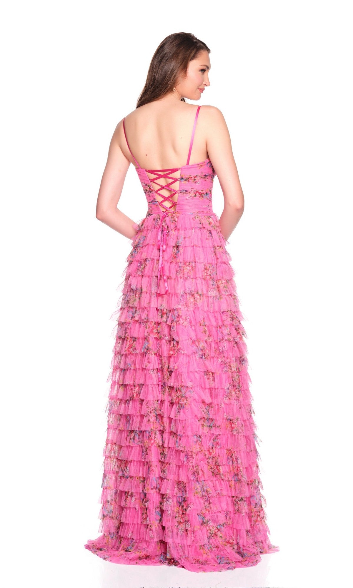 A woman faces away, modeling the Dave and Johnny 12685 long prom dress in fuchsia pink with a tiered A-line tulle skirt, delicate floral patterns, and lace-up back detail against a white background.